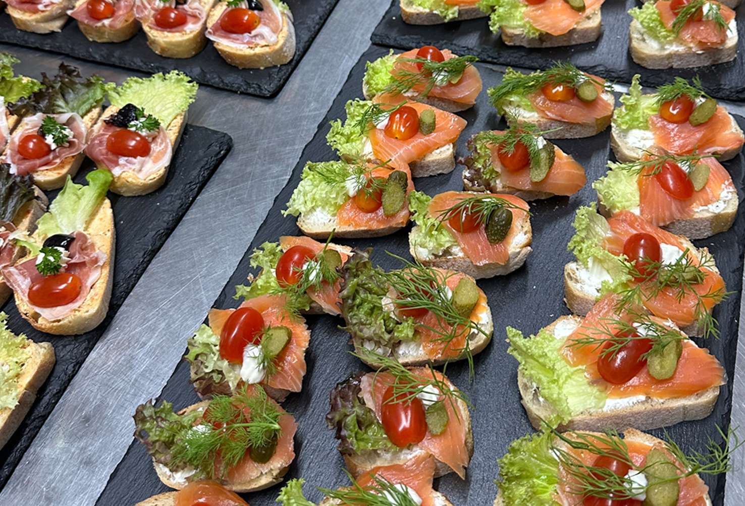 Reihen von Lachs- und Schinkenhäppchen auf Schieferplatten