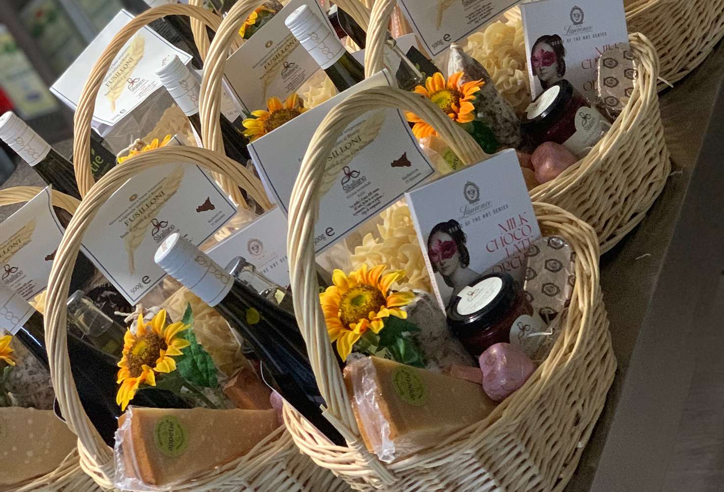Mehrere Feinkost-Geschenkkörbe mit Pasta, Wein und gelben Blüten