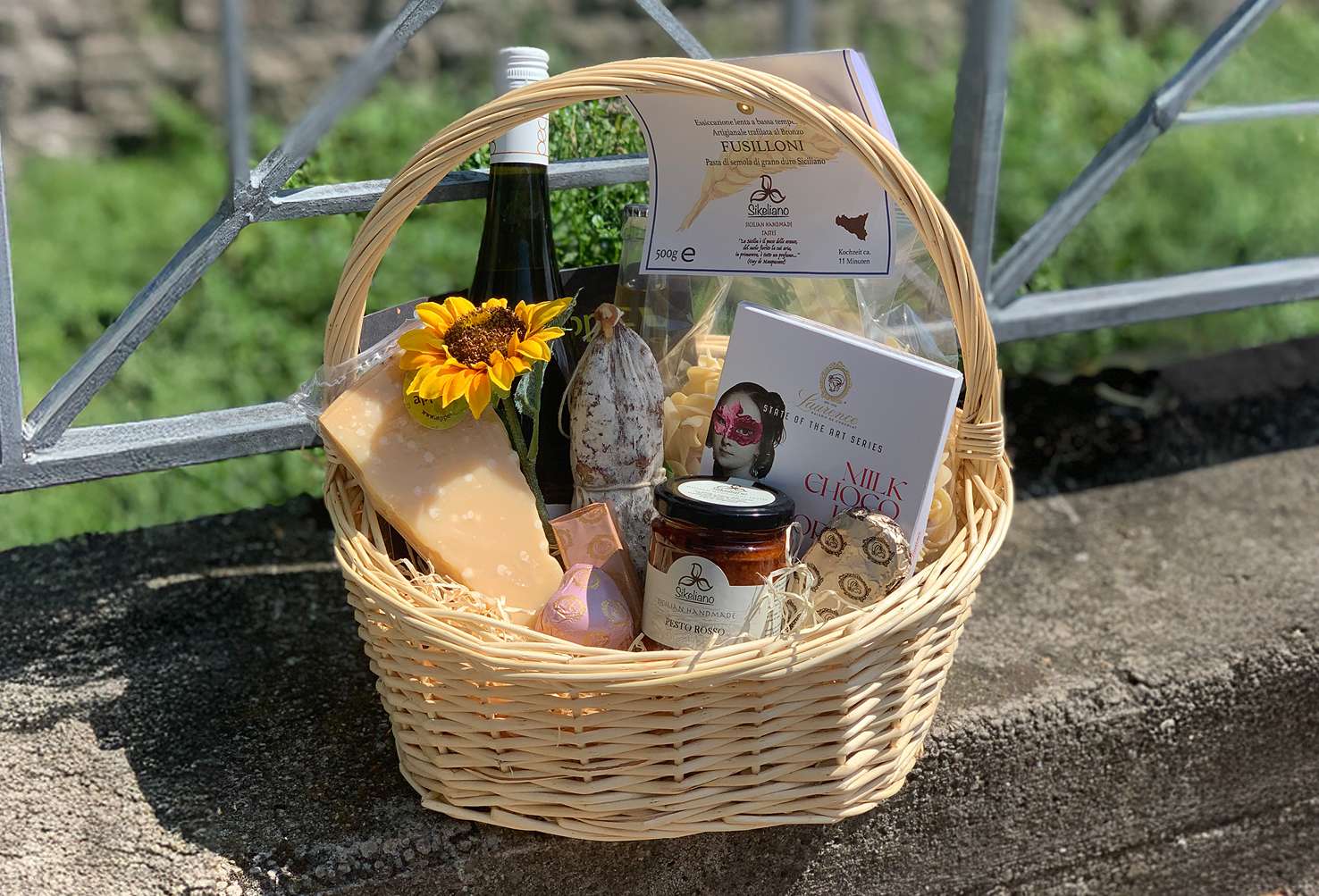 Geschenkkorb mit Pasta, Käse, Salami und Aufstrich, dekoriert mit gelben Blüten